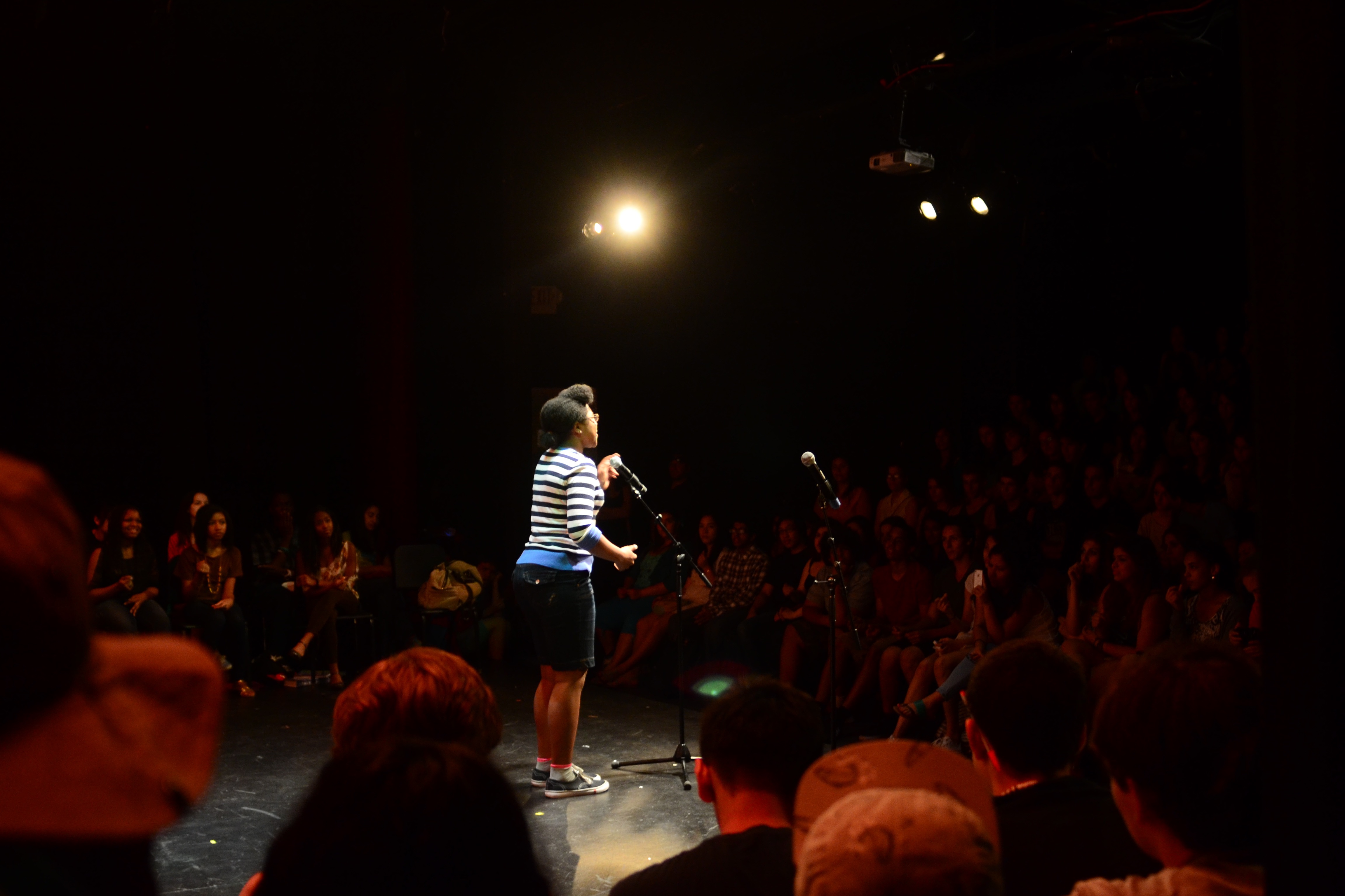 Aaleah performing spoken word at Word Up! under a single overhead stage light.